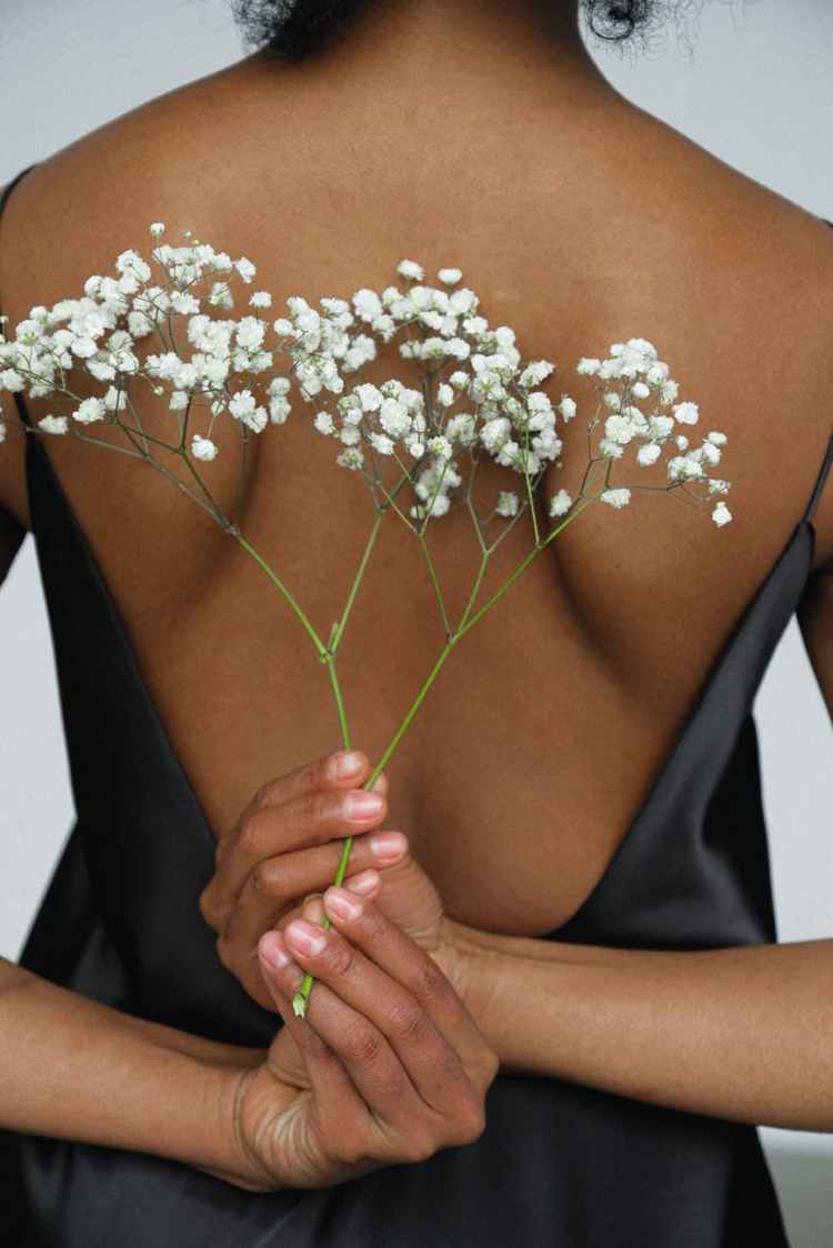 close up photo of woman in black night dress holding white flower behind her back